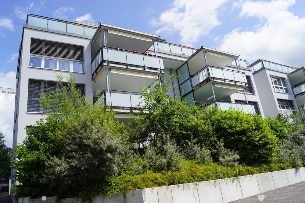 Multistory residential building, multiple balconies, white exterior, glass windows, greenery at the base