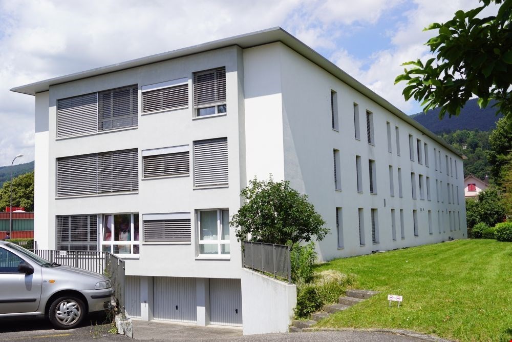 Modern three-story white building, two garages in the ground floor, car parked in front