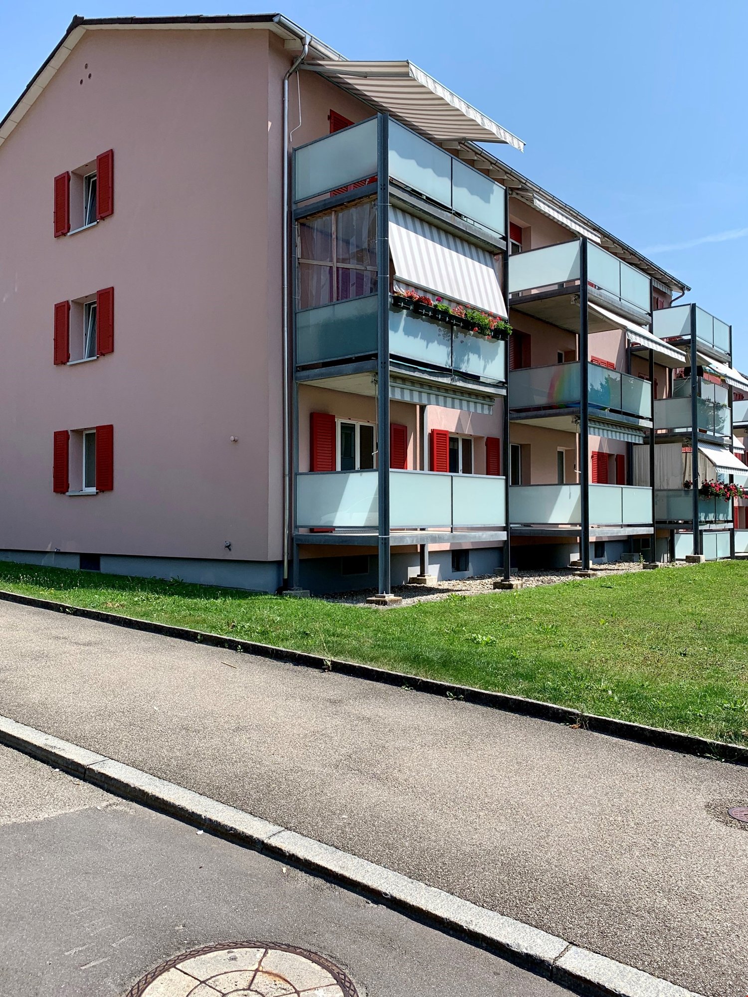 Two-story apartment building, brick exterior, red shutters, multiple balconies, awnings