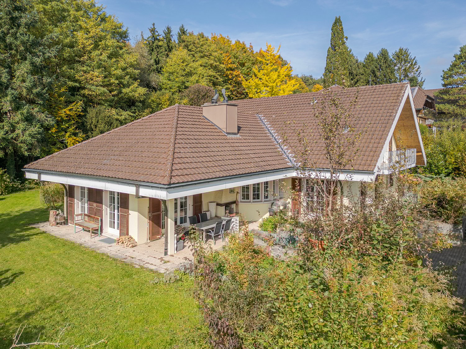 Detached house, brown roof, white walls, large windows, outdoor dining area, balcony, lush greenery