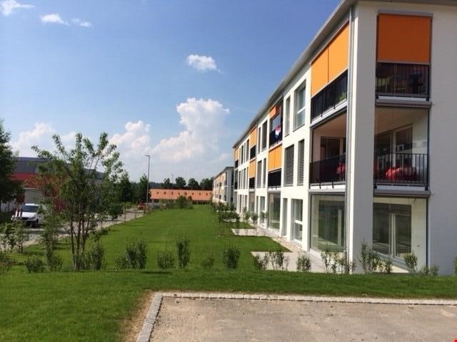 modern multi-story building, white and orange exterior, balconies, grass lawn, plants