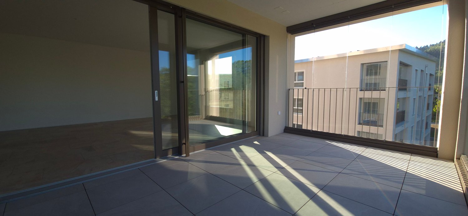 Balcony with sliding glass doors, tiled floor, metal railing, view of another building and trees