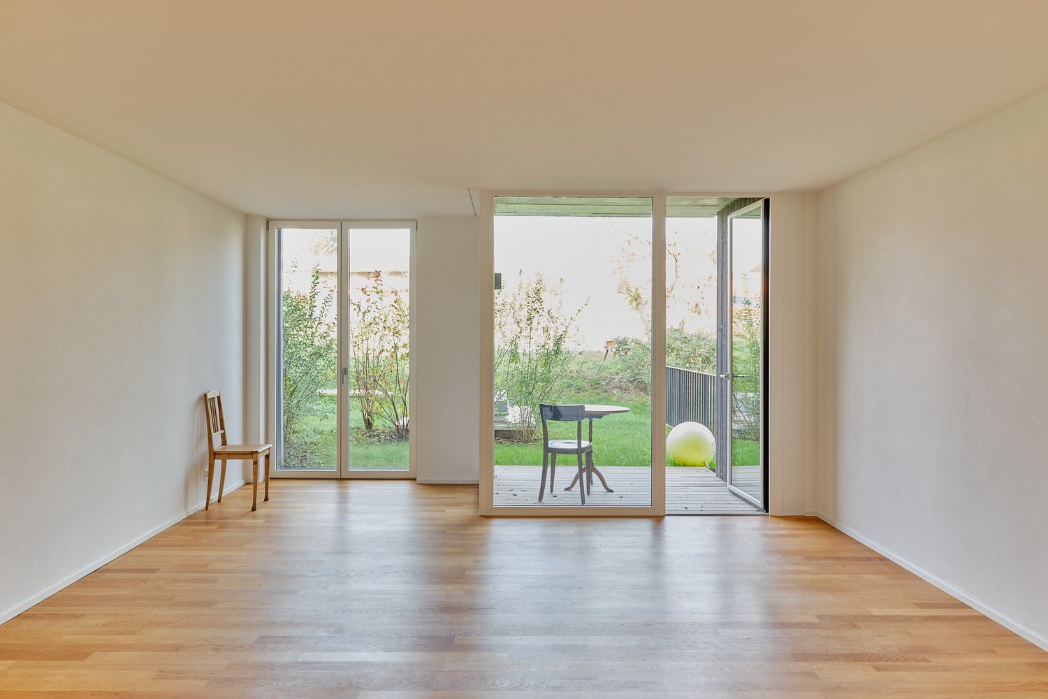 white walls, hardwood floor, double glass door, sliding glass door, table, chairs, balcony, green lawn