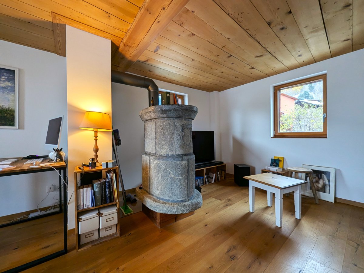 Cozy living room with wooden ceiling, stone fireplace, desk with computer, bookshelves, and a small table with chairs.