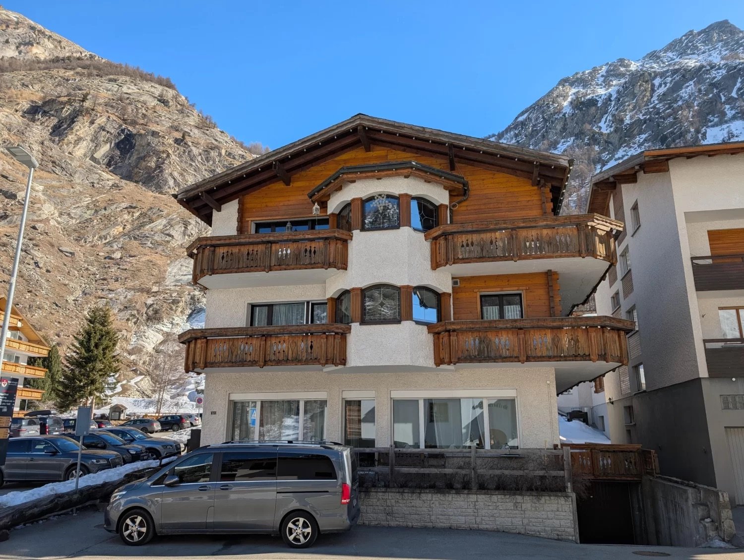 Three story building, wooden balconies, white walls, gray trim, glass windows, snow-covered mountain in the background