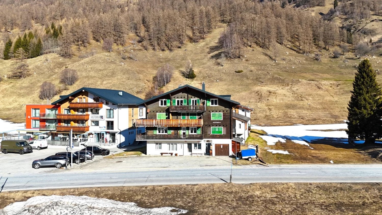 Multi-story building with apartments, balconies, and a parking area in a mountainous, forested landscape