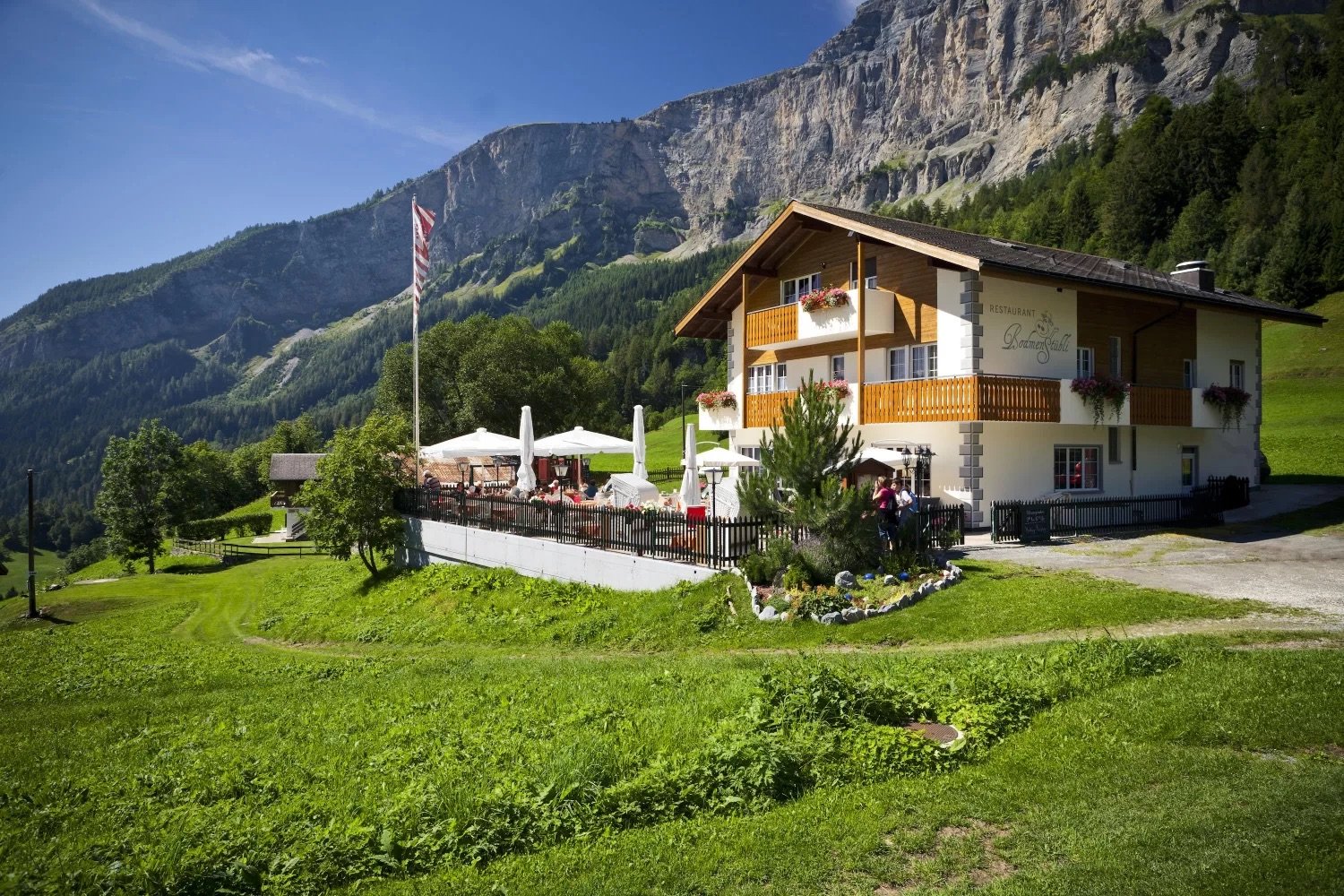 Traditional Swiss chalet with restaurant, balcony with tables, flag, surrounded by grass and mountains