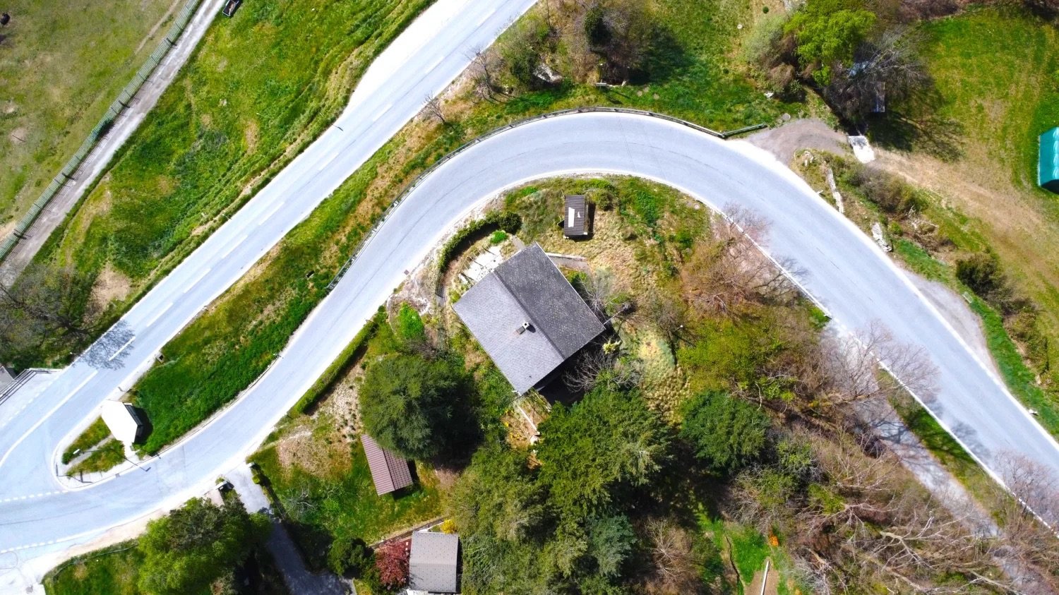 Aerial view of a house surrounded by lush green vegetation, with a winding road passing by the property.