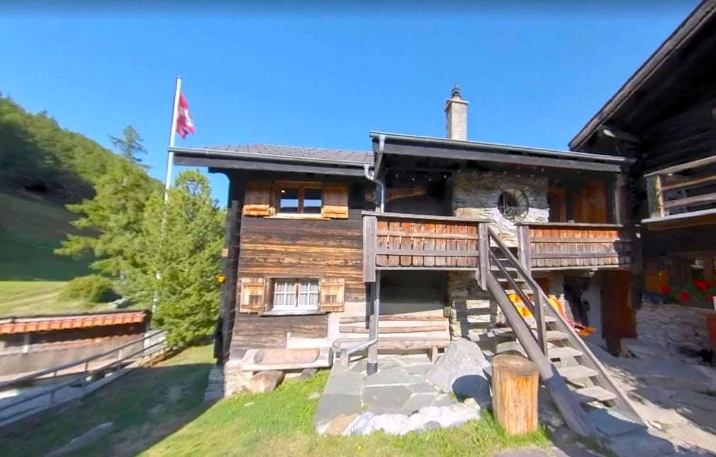 2-story wooden chalet-style house, with a balcony and porch, surrounded by trees and greenery