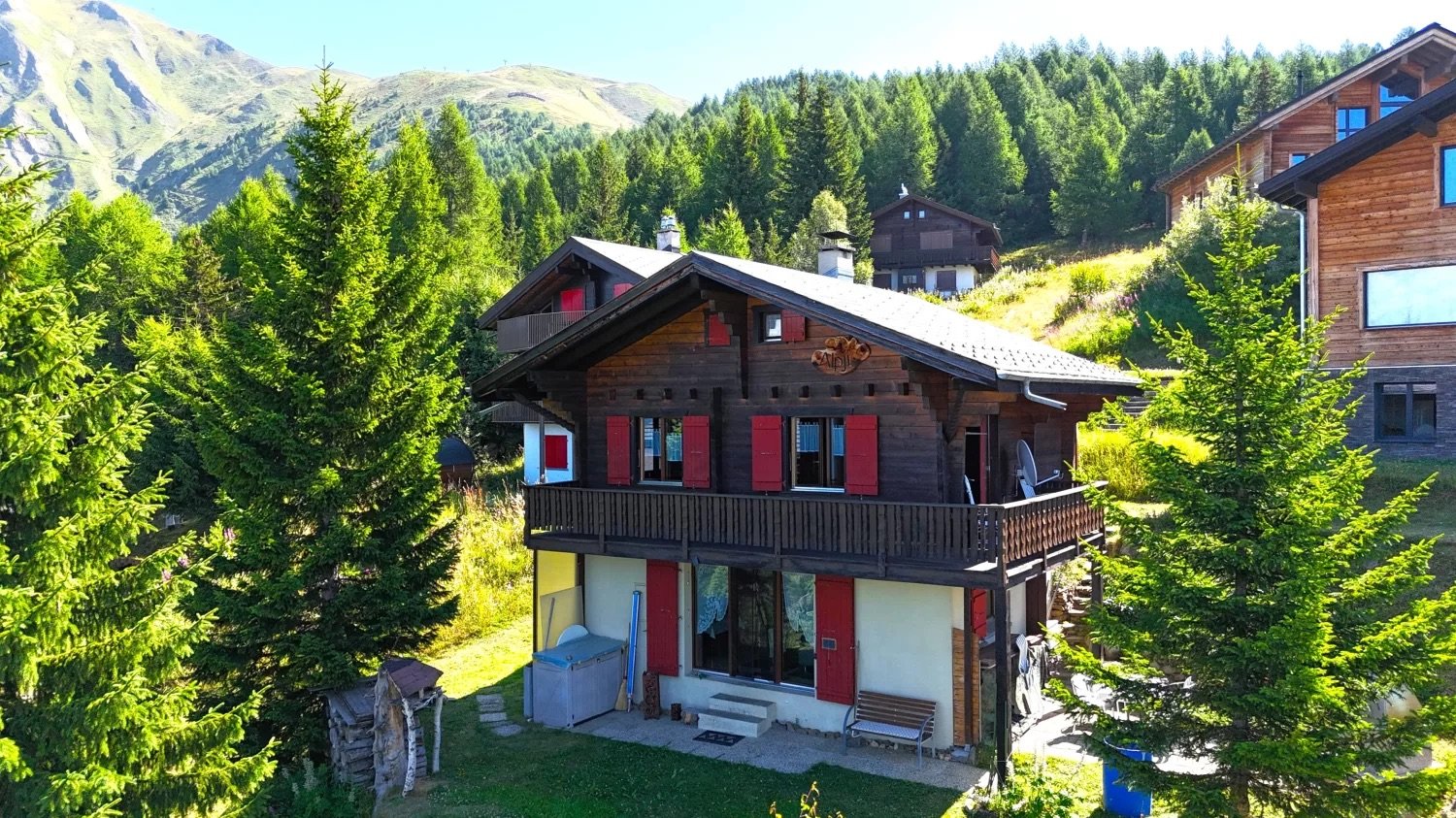 two story chalet, red shutters, wooden terrace, lawn, mountain view