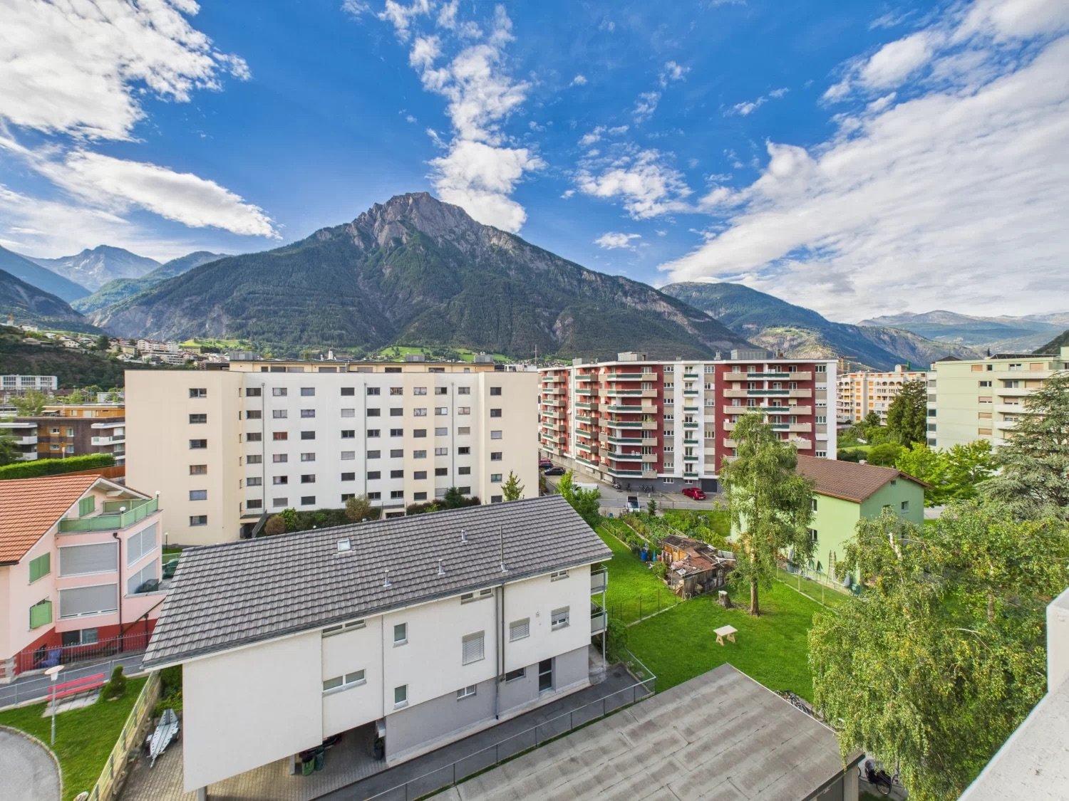 Aerial view of multiple residential buildings with mountainous background, one building has a parking area