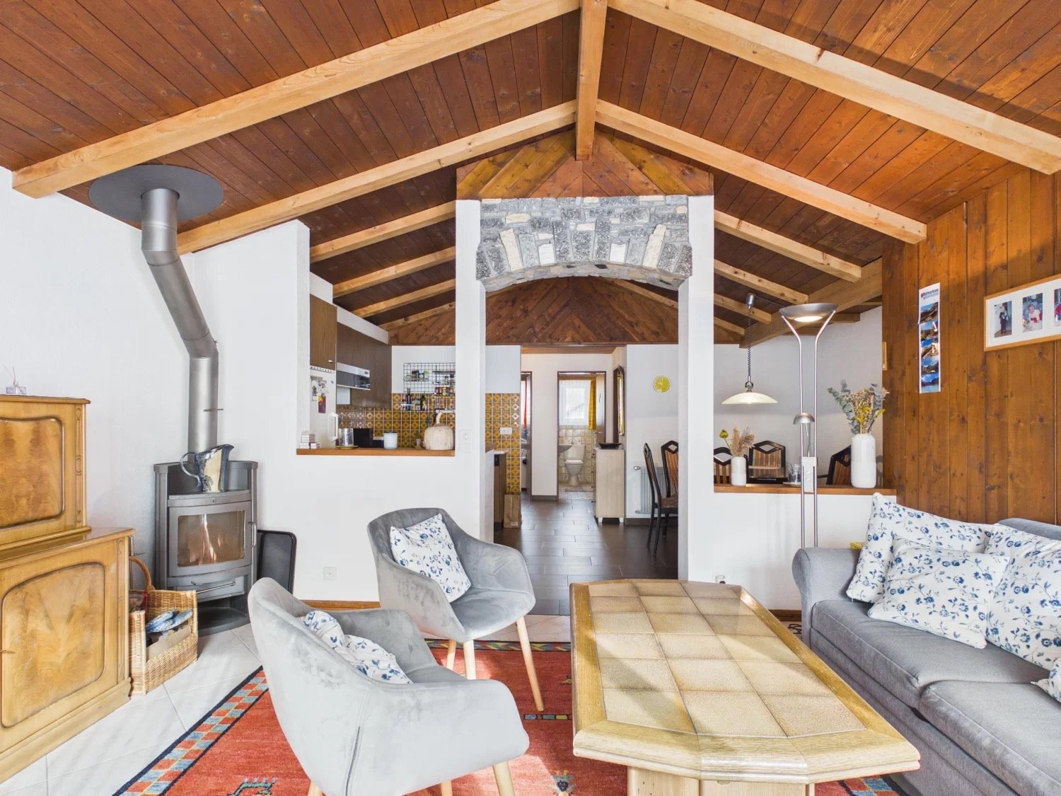 wooden ceiling, fireplace, wooden floor, gray couch, wooden coffee table, wooden chairs, wooden cabinet, basket, radiator