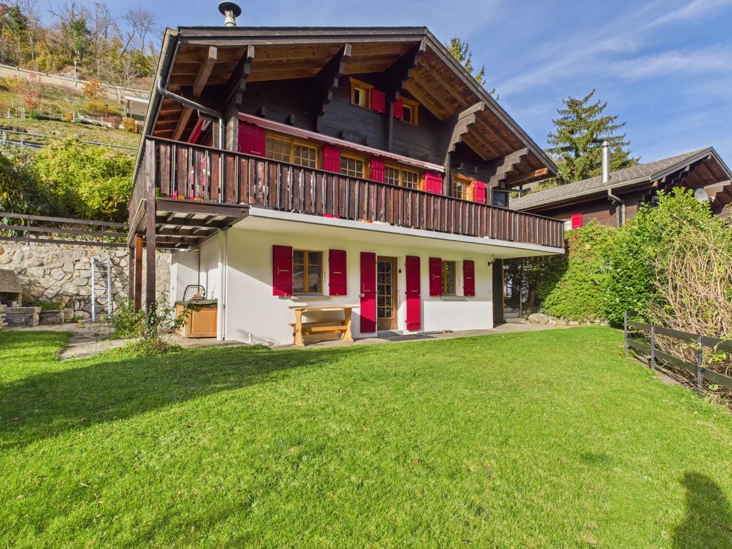 2 story chalet, wooden balcony, red shutters, white walls, wooden bench, wooden storage box, well-maintained lawn
