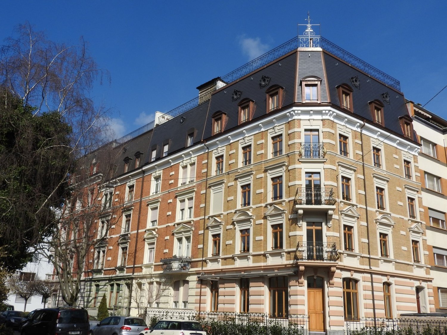 large multistory building with balconies, black roof, white and brown facades, windows with shutters