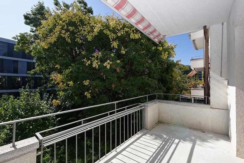 Terrace with metal railings and shaded area, overlooking trees and buildings.