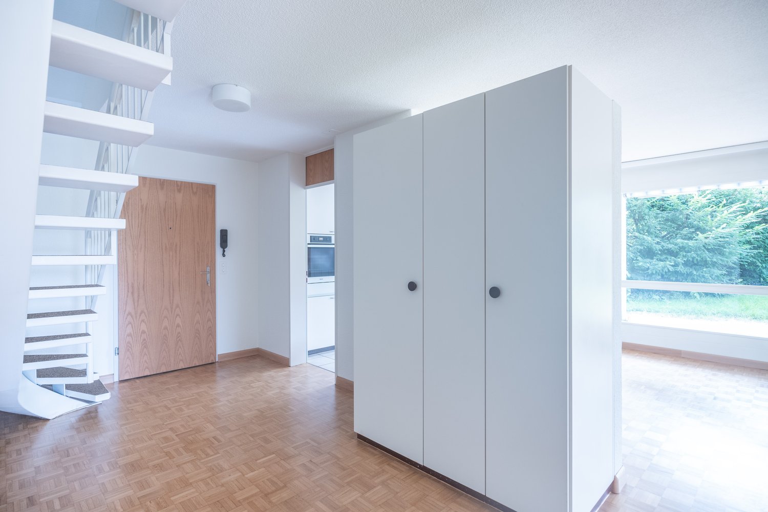 white wall, wooden floor, spiral staircase, white built-in closets, door, window, corridor