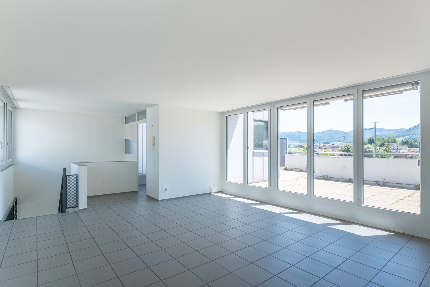 Empty room, large windows, tiled floor, bright light, balcony, white walls, door