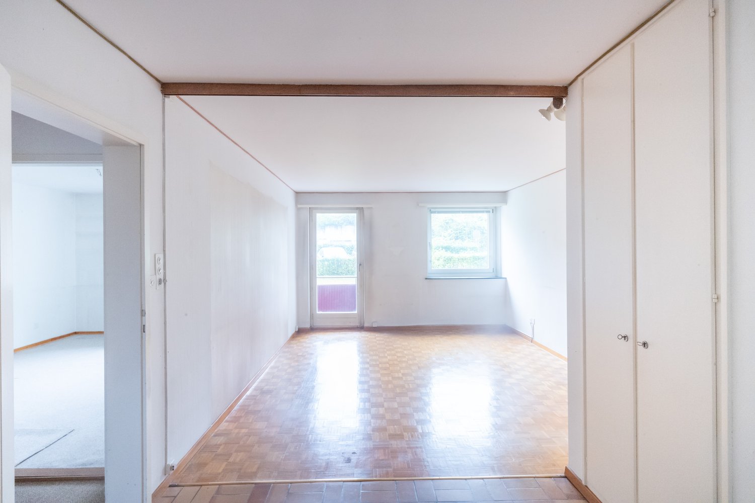 Empty room, white walls, wooden floor, two windows, one with an exit
