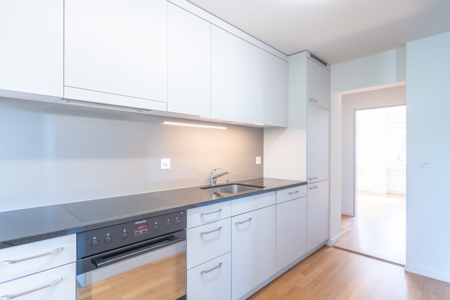 White cabinetry, black countertops, stainless steel sink, induction cooktop, dishwasher, electric oven