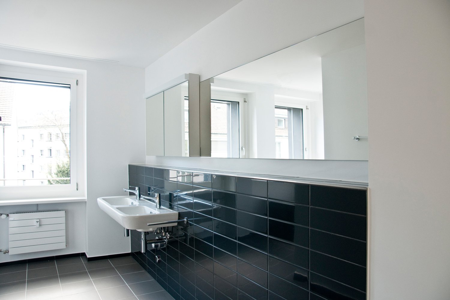 Large mirror, white sink, black tiles, window