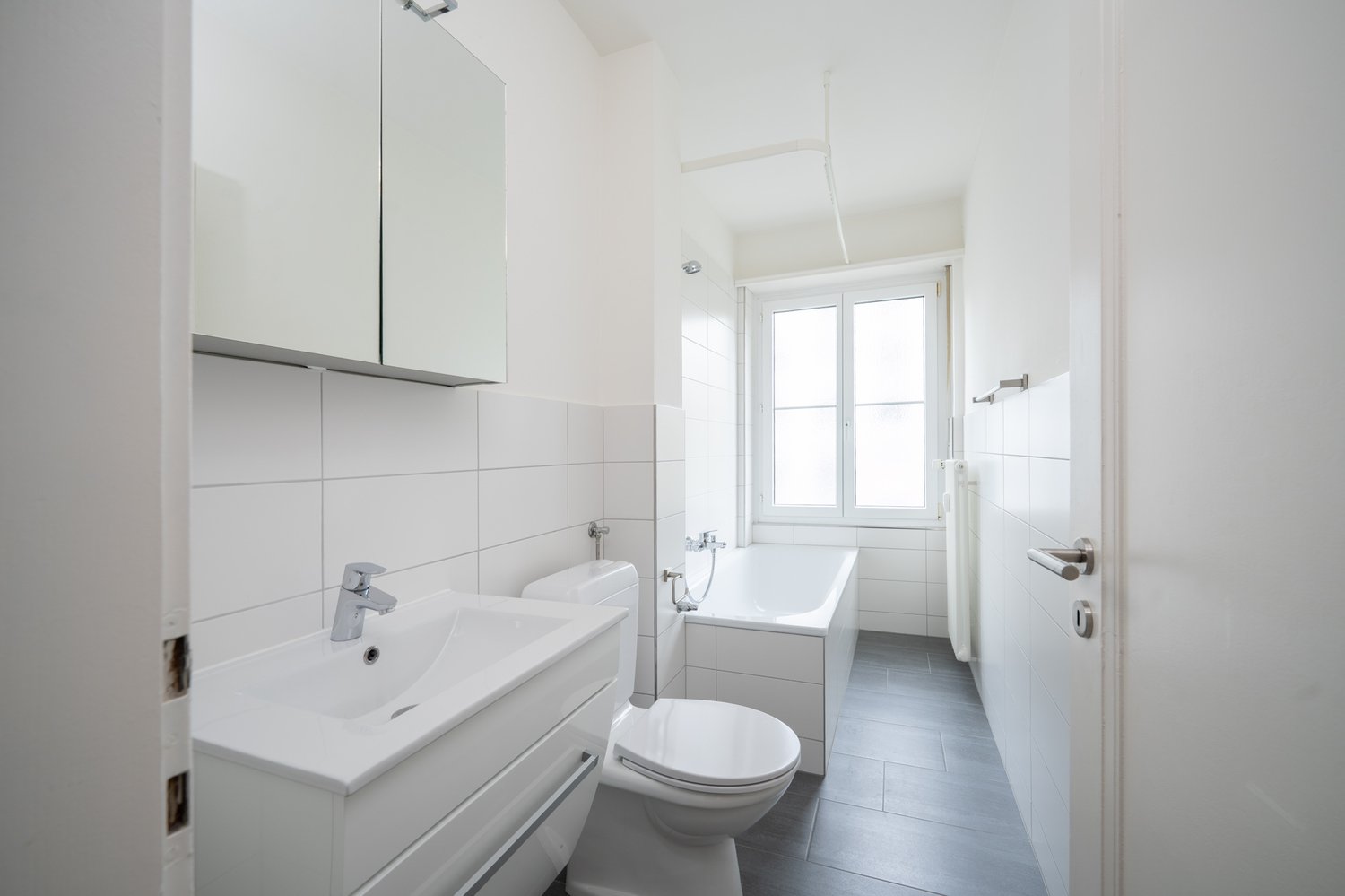 Bathroom with white tiles, white sink, white toilet, bathtub, mirror, and window