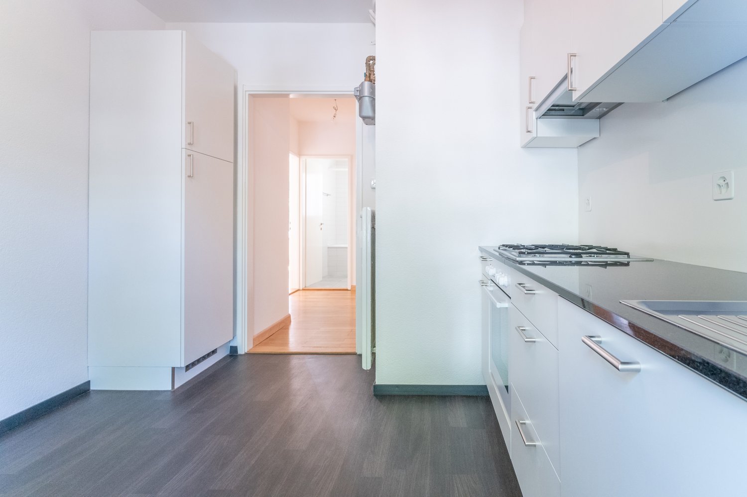 modern kitchen with white cabinets, wooden floor, gas stove, sink, and a door leading to another room