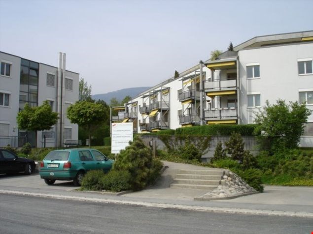 White multi-storey residential building with balconies, a green car parked in front of it