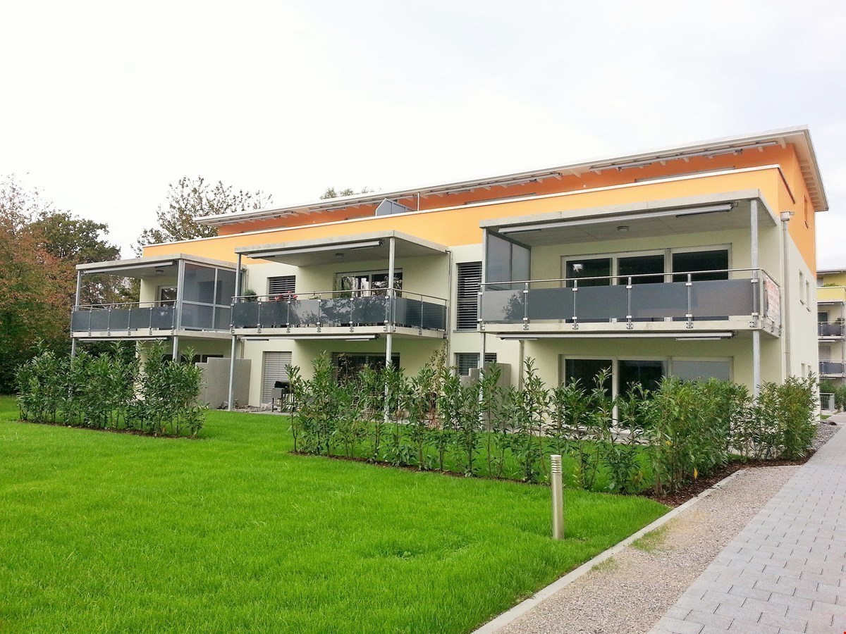 Two-story apartment with yellow exterior and white walls, balconies, well-manicured garden, paved pathway