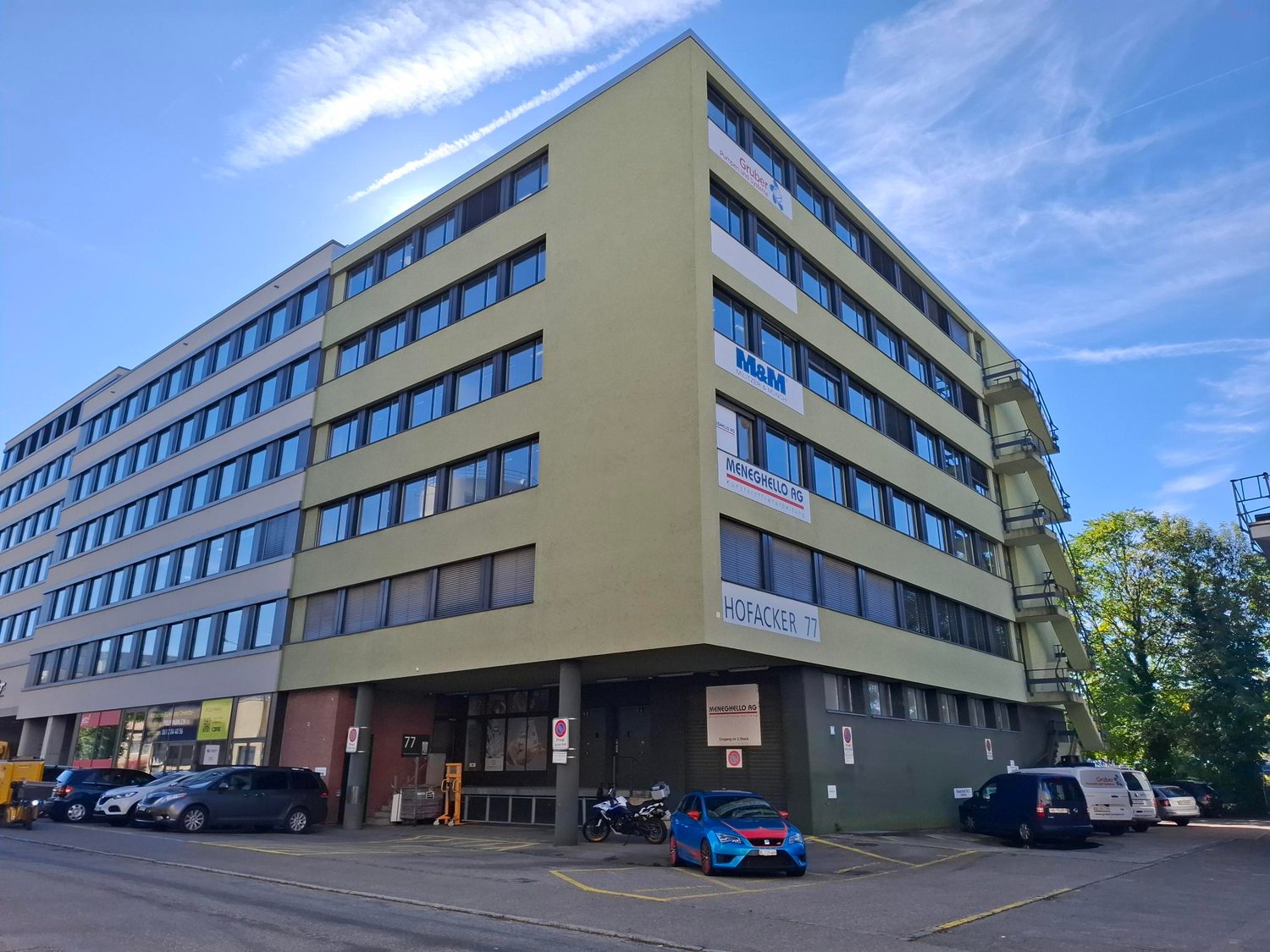 Office building, 3 floors, multiple windows, parking lot, motorcycles and cars parked