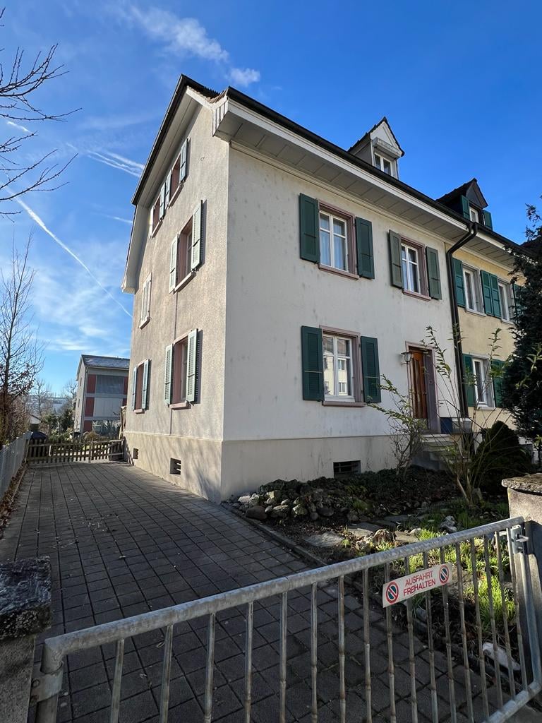 3-story white building, with tiled driveway, green shutters, and small garden