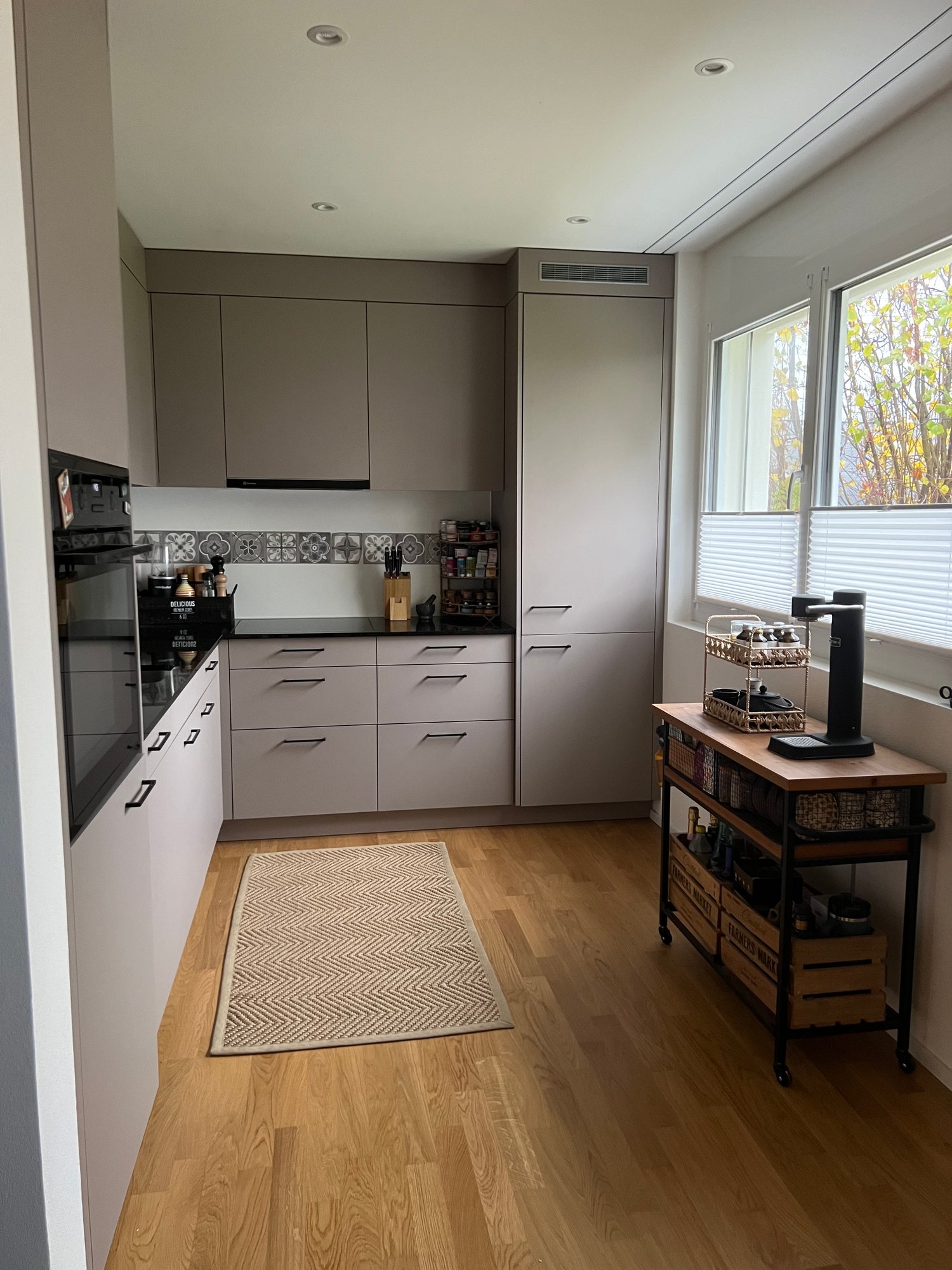 Modern kitchen with oak flooring, white cabinets, black countertops, built-in appliances, pantry, spice rack, open shelving, large windows