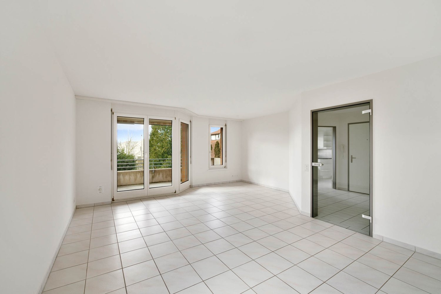 Empty room, white tiles, glass doors leading to balcony, windows, white walls, glass doors to other room