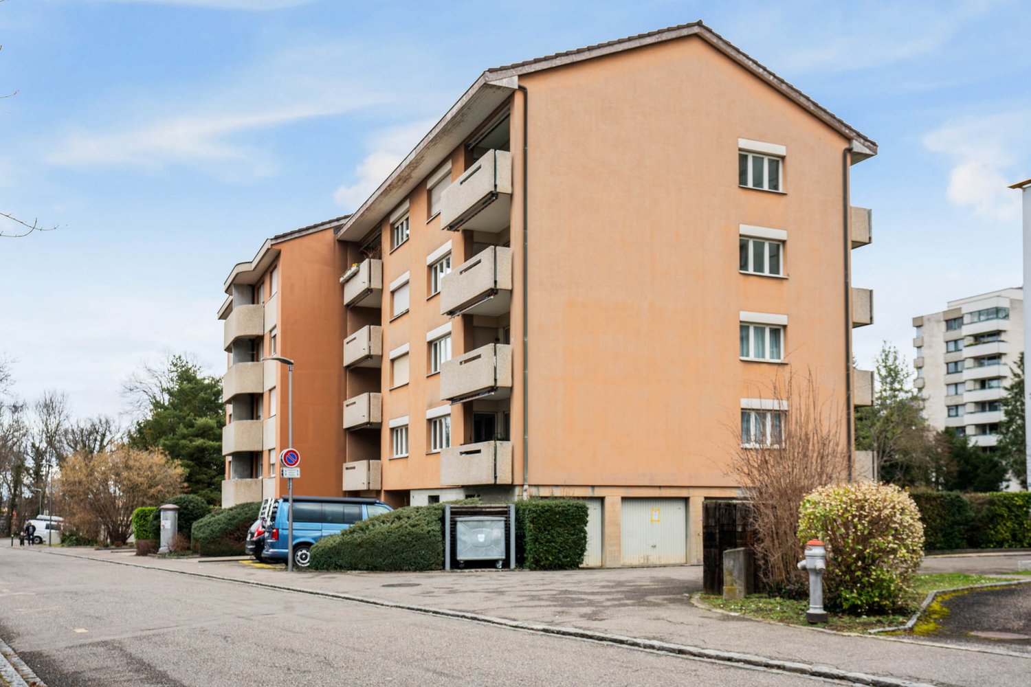 Modern, beige apartment building with multiple balconies, two garages and street parking spaces.