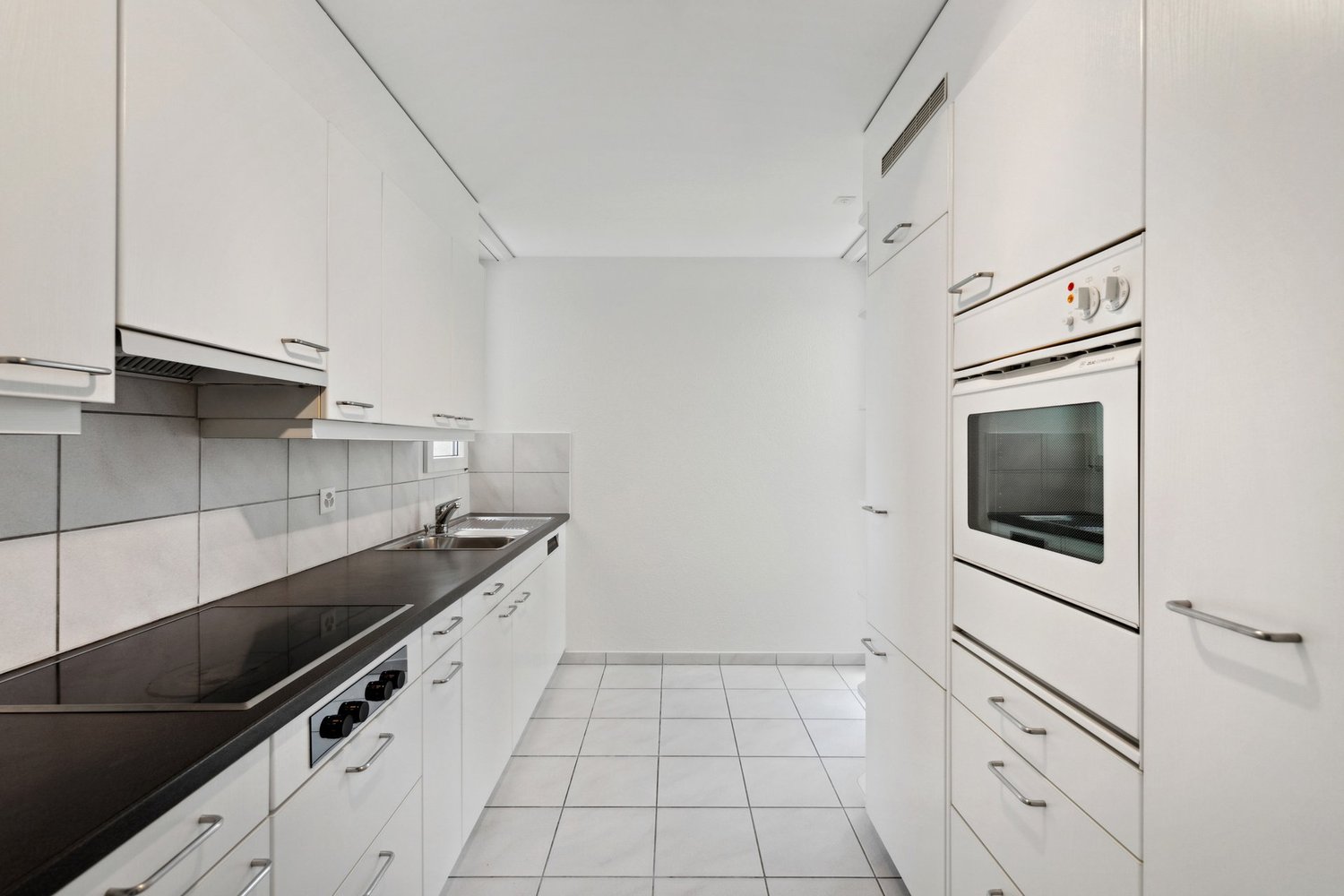 Modern kitchen with white cabinets, black countertops, built-in oven, dishwasher, gas stove, and sink.