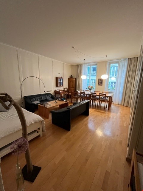 large open living space with a dining area, wooden flooring, white walls, two couches, a sofa bed, a coffee table, a wooden cabinet, a wooden table, and chairs