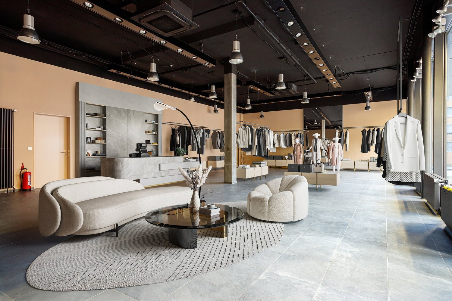 Large open space with concrete floors, black ceiling with track lighting, display racks and shelves for clothing, a curved white sofa and coffee table in the center, and a reception desk at the back of the store.
