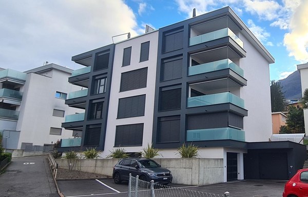 4-story modern apartment building with glass balconies, parking spaces in front