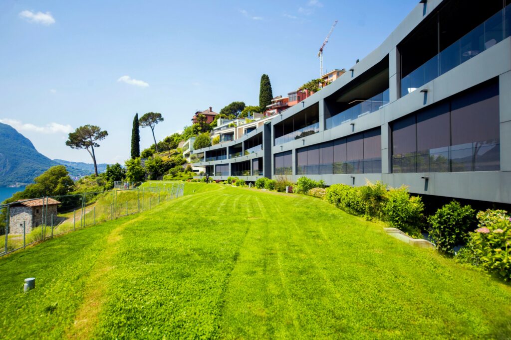 modern apartment complex on hillside, large green lawn, fenced area, glass balconies