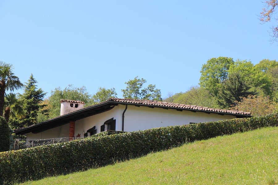 white house, terracotta roof, small balcony, white chimney, green hedge, grassy hill