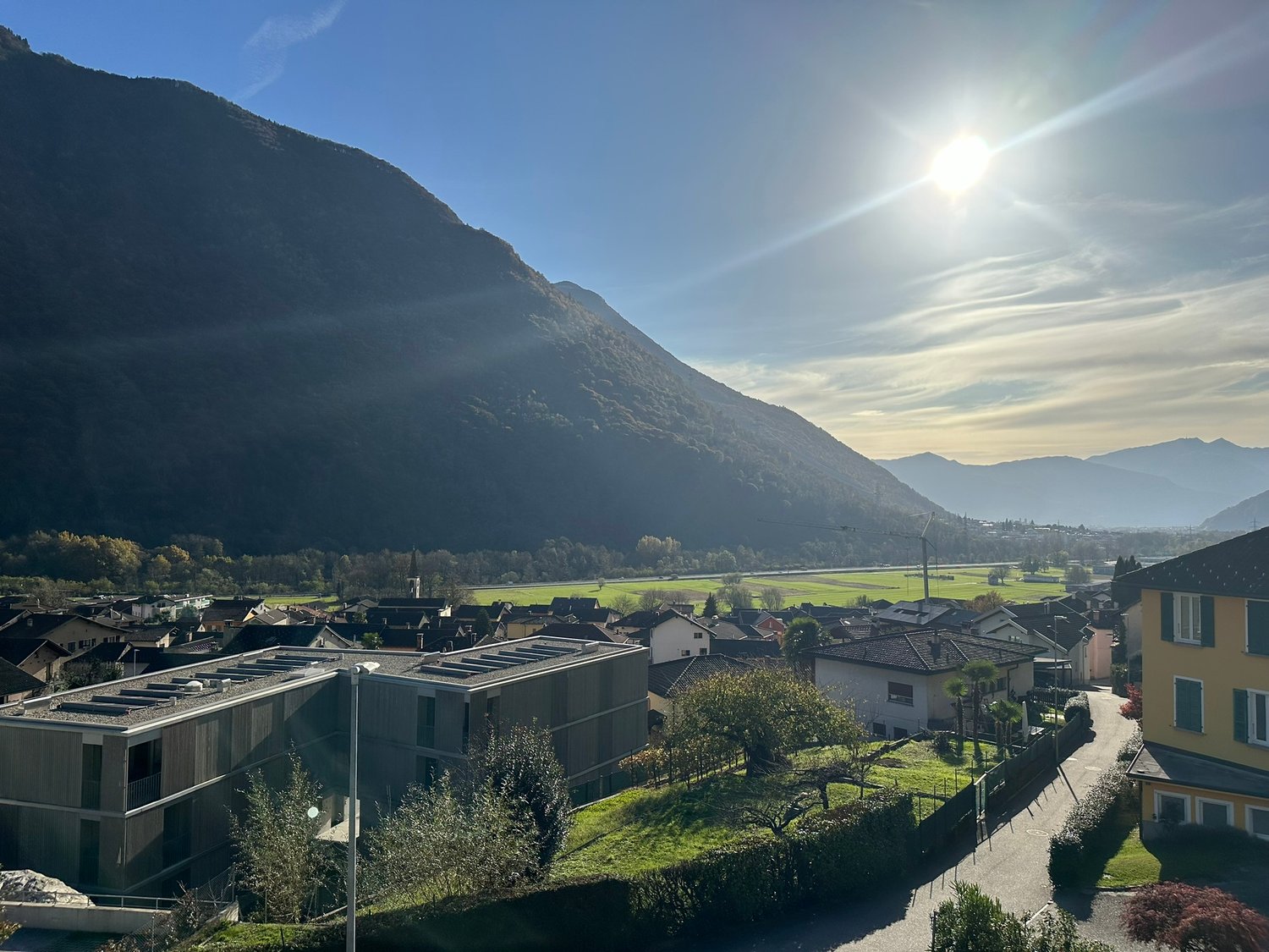 House exterior, large windows, flat roof, modern architecture, solar panels, surrounded by green grass, view of a valley, mountains in the background