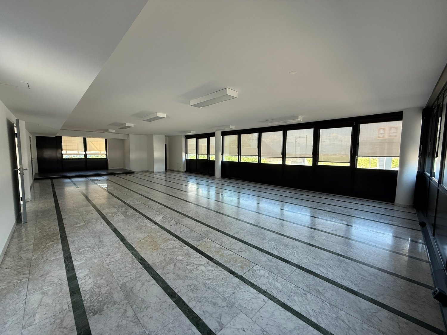 Large open space with marble flooring, floor-to-ceiling windows, and recessed lighting. The room appears to be a multipurpose space, potentially used for events or activities.