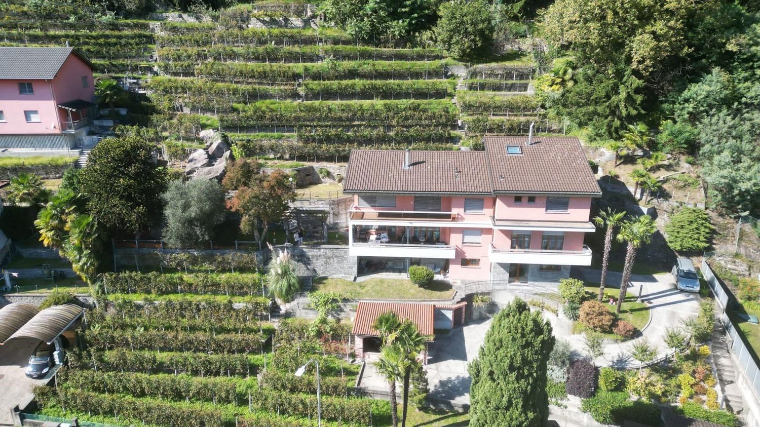 Two story house, terracotta roof, balcony, garage, surrounded by terraced fields and greenery