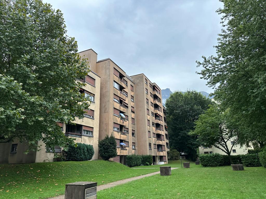 An apartment building with multiple stories, balconies, trees, and a well-maintained lawn in front.