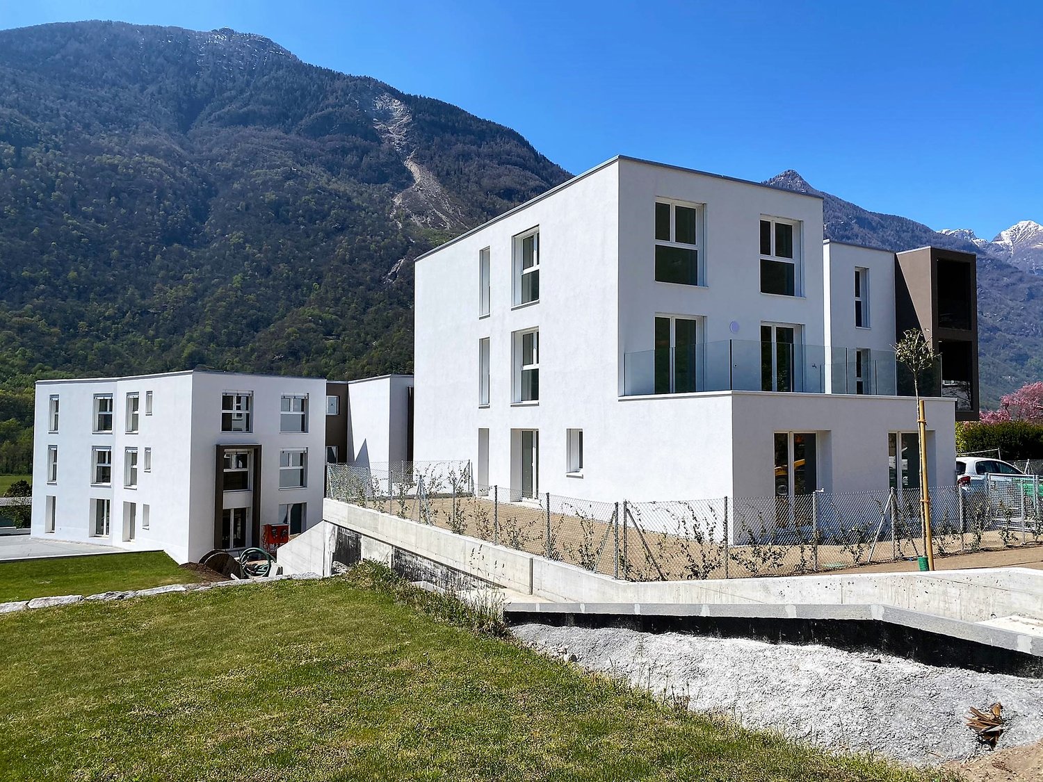 White apartment building, modern design, concrete driveway, green lawn, mountains in the background