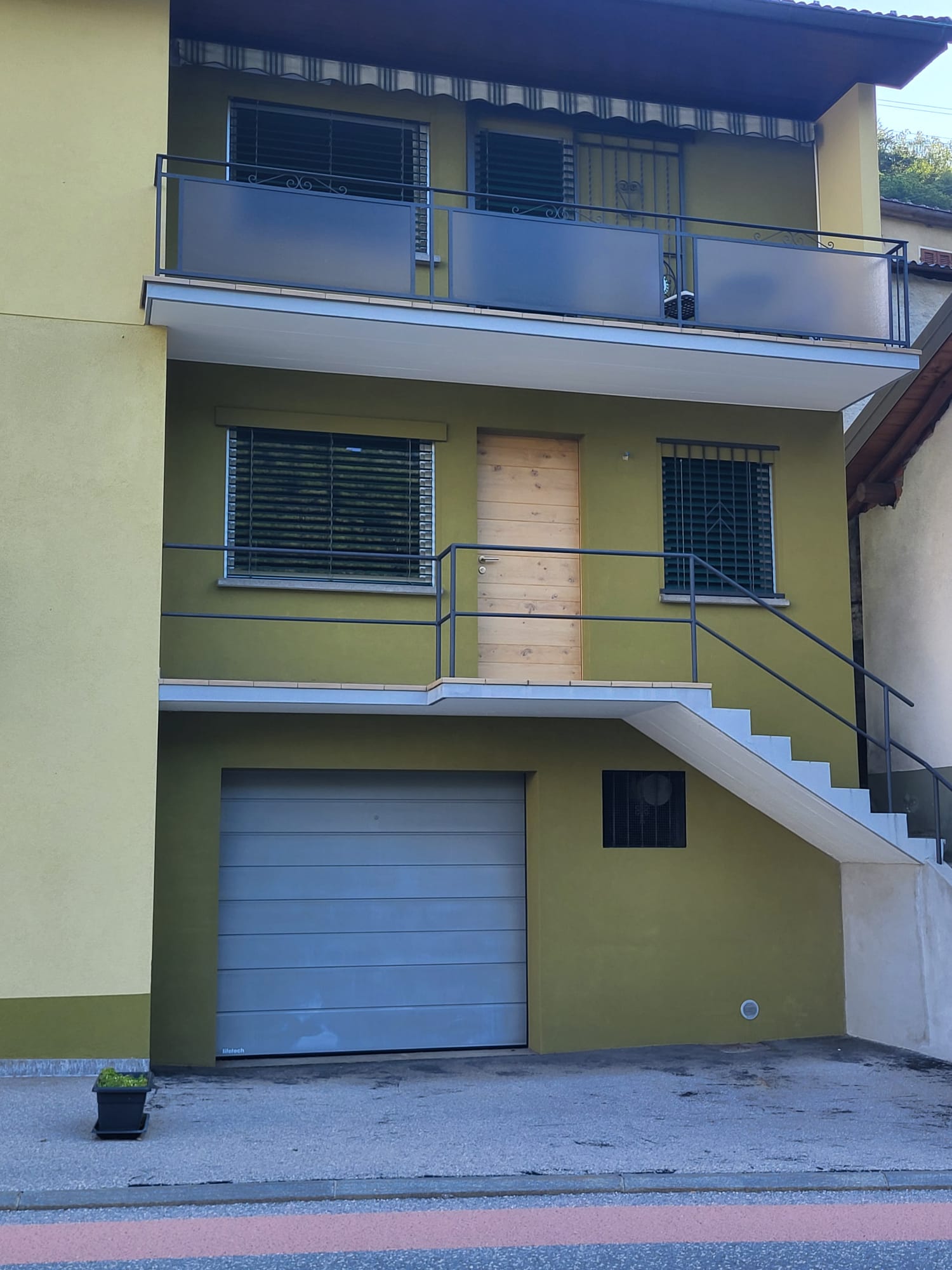 2 story house, yellow exterior, metal railings, wooden door, garage, balcony