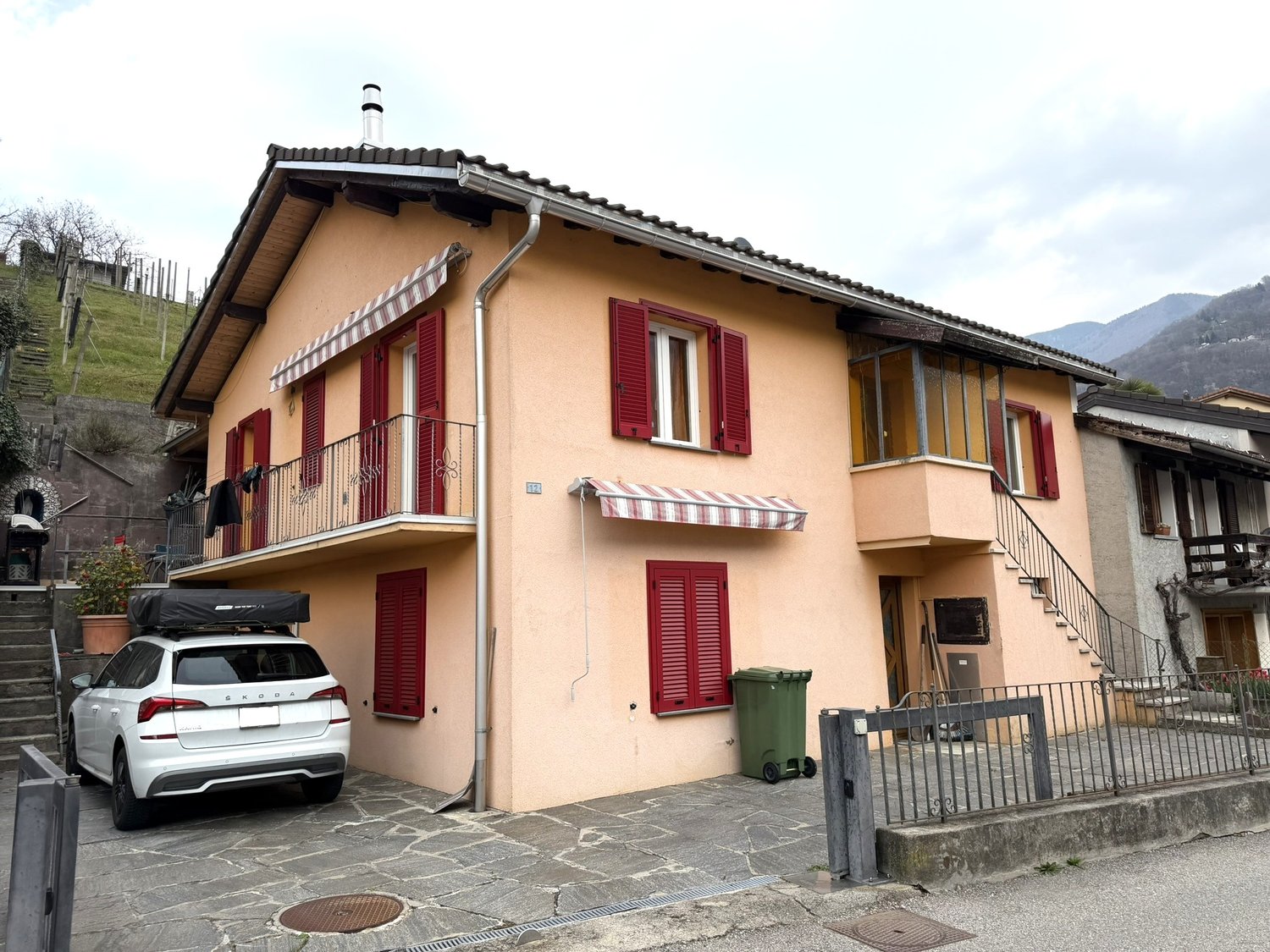 Two-story house, beige exterior, red shutters, balcony, car parked in front