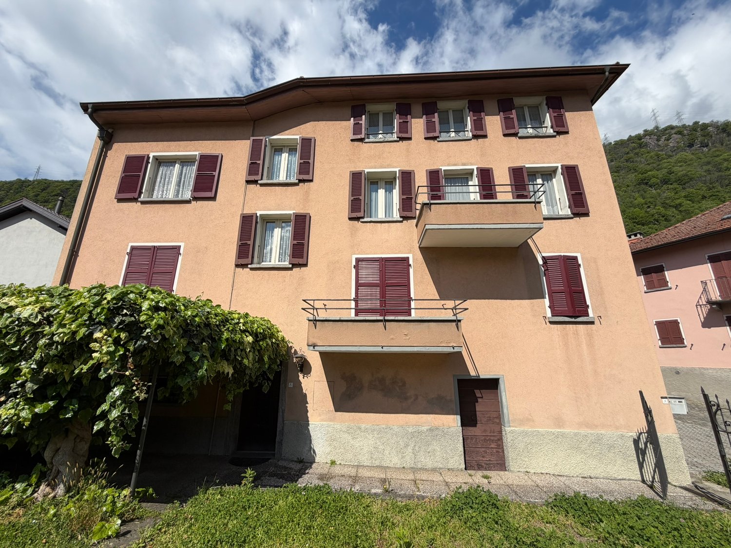 3 story building, beige exterior, red shutters, balcony, garage, green vegetation