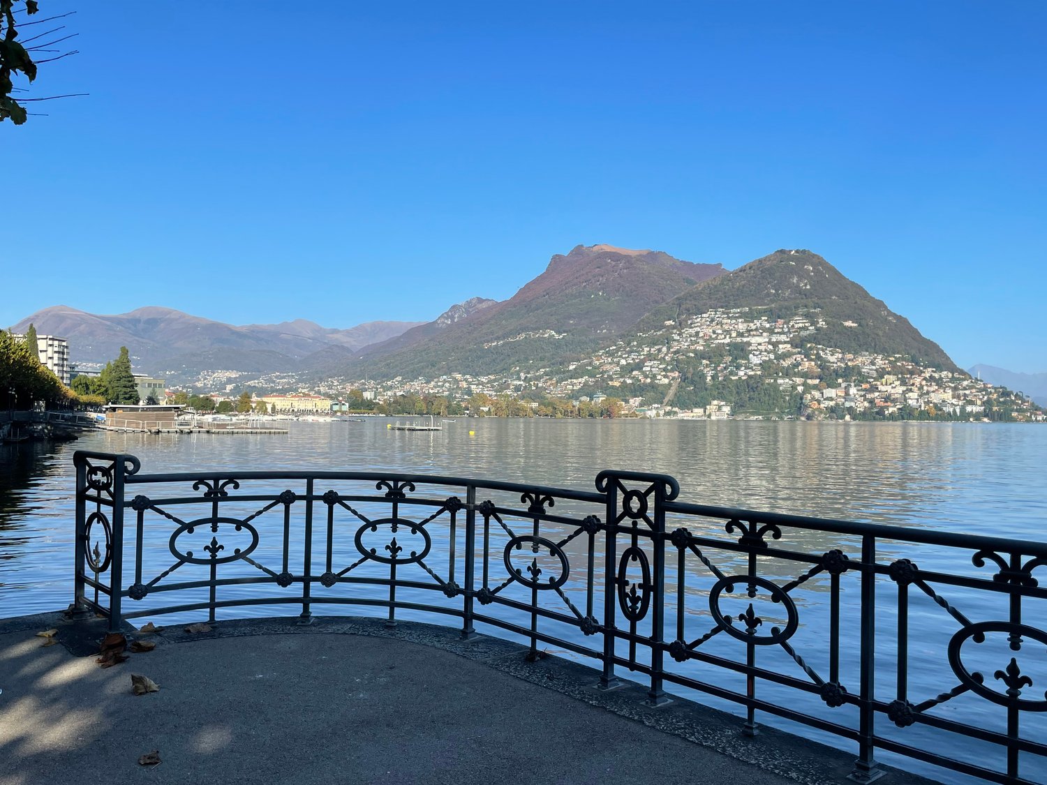Panoramic view of a lake with mountains in the background, a fence and a town