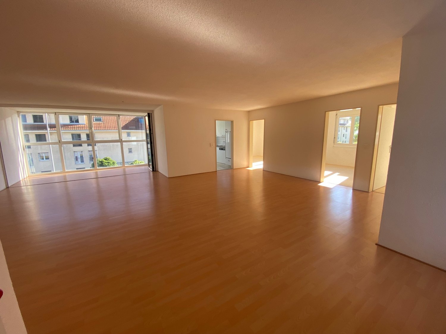 Empty room with wooden flooring, large windows, and open doorways leading to other spaces.