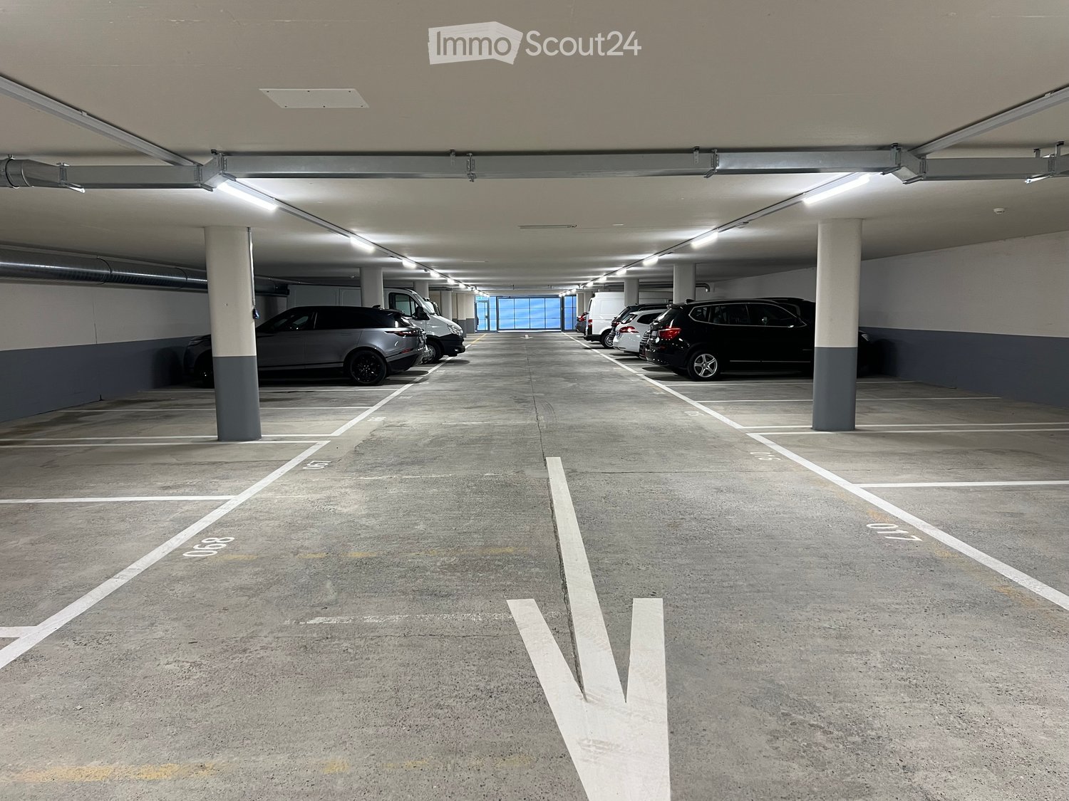 A parking garage with a ceiling, multiple parking spots, and a few vehicles parked.